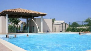 A swimming pool with a covered area, a clear sky, and a fenced area with people and a building in the background. - Charming air-conditioned house in Sorède sleeps 4/6, 6 km from Argelès Sur Mer. (Sorède)
