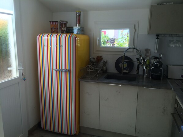 A kitchen with a striped refrigerator, a window with a view of greenery, and a sink with various utensils. - Charming, air-conditioned house in Sorède for 4–6 people, 6 km from Argelès-sur-Mer. (Sorède)