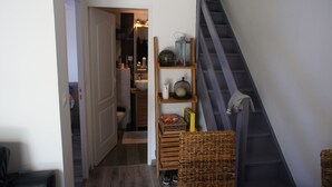A narrow hallway with a staircase on the right, leading to a second floor. There are wicker baskets on the floor and a shelf with various items including a lamp, a box, and a decorative bowl. - Charming air-conditioned house in Sorède sleeps 4/6, 6 km from Argelès Sur Mer. (Sorède)