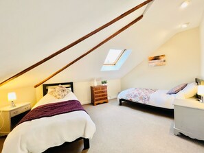 A bedroom with a sloped ceiling, a skylight, a bed with a floral bedspread, a dresser, and a bedside table with a lamp.