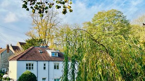 A white two-story house with a red-tiled roof, surrounded by trees and a fence. - Central Bristol/Bath both 9 mins by train - by river, park in Conservation Area (Keynsham)