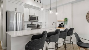 A modern kitchen with white cabinetry, stainless steel appliances, a central island with bar stools, and pendant lighting.
