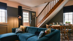 A cozy living room with a blue sectional sofa, a wooden staircase, and a dining area with a table and chairs. - Waverley (Lyme Regis)
