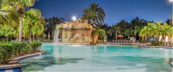 Relax by the serene pool surrounded by lush tropical vegetation and a stunning rock formation with a cascading waterfall.