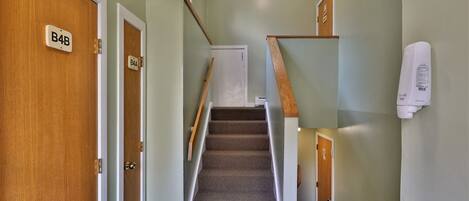 A staircase with carpeted steps, wooden handrails, and a white wall with a thermostat.