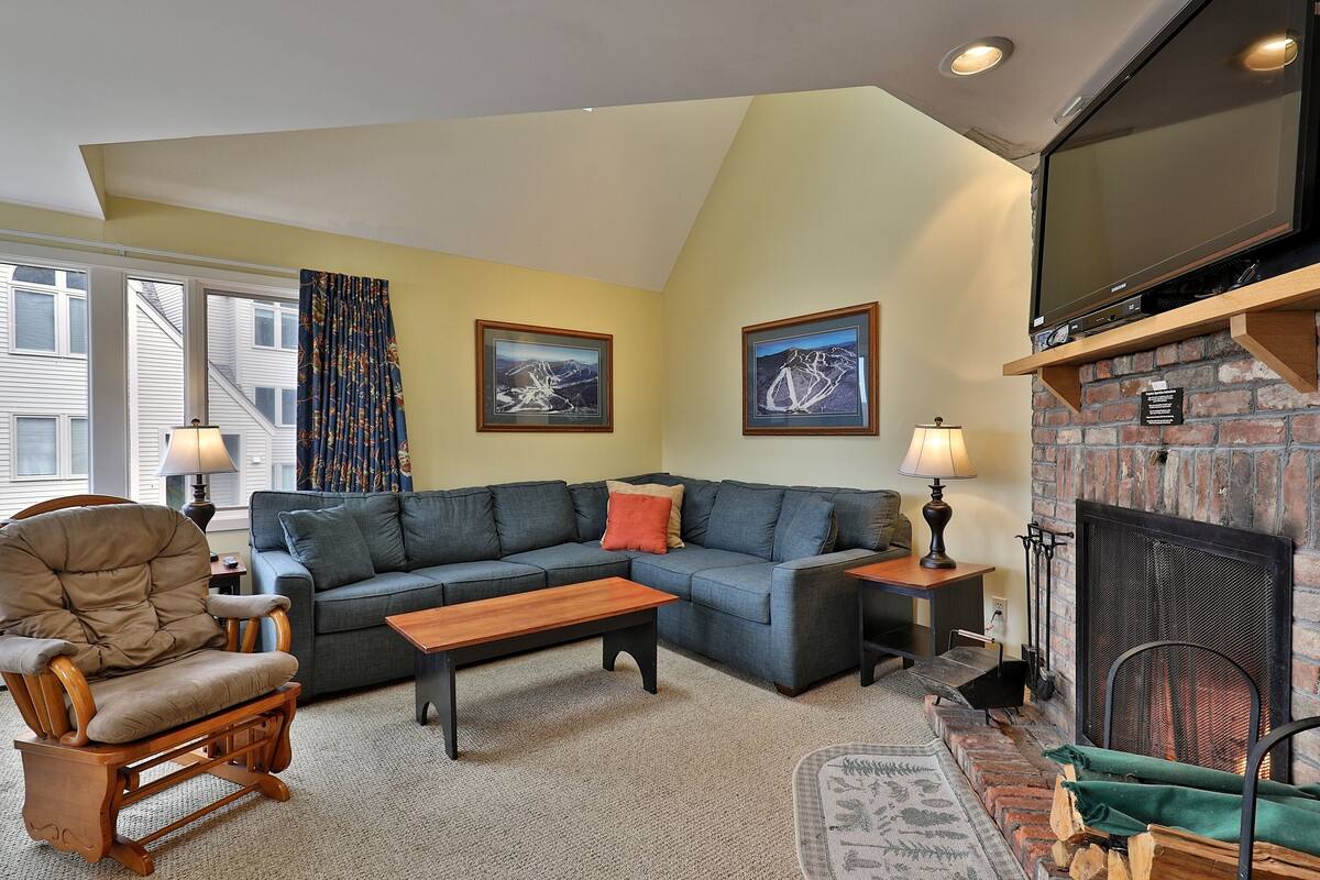 A living room with a sectional sofa, a rocking chair, a fireplace, and framed pictures on the wall.