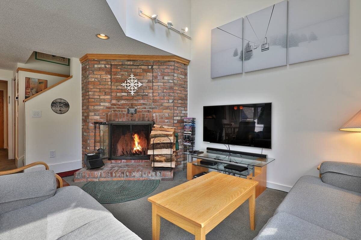 A living room with a brick fireplace, a flat-screen TV, and a staircase leading to another level.