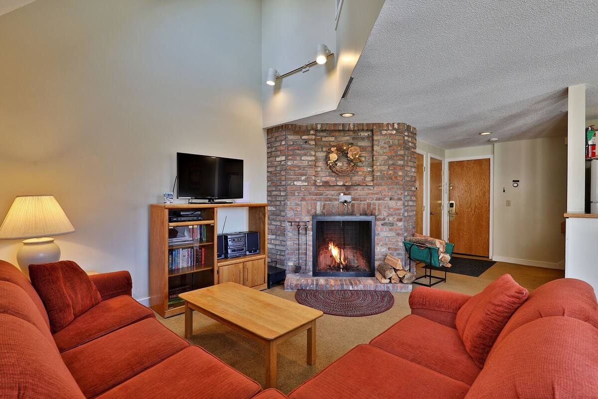 A living room with a fireplace, red sofas, a coffee table, and a television.