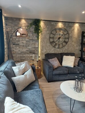 A modern living room with a grey sofa, a round coffee table, and a large wall clock.