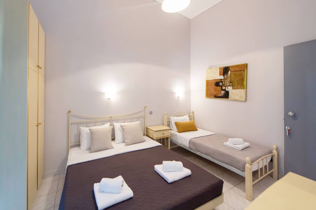 Habitación de hotel con dos camas, una mesita de noche, un armario y un cuadro.