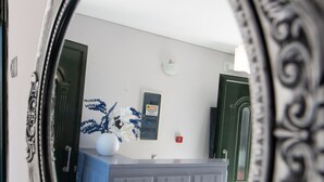 A mirror reflecting a room with a blue cabinet, a white vase, and a door. - George House (Lefkada)