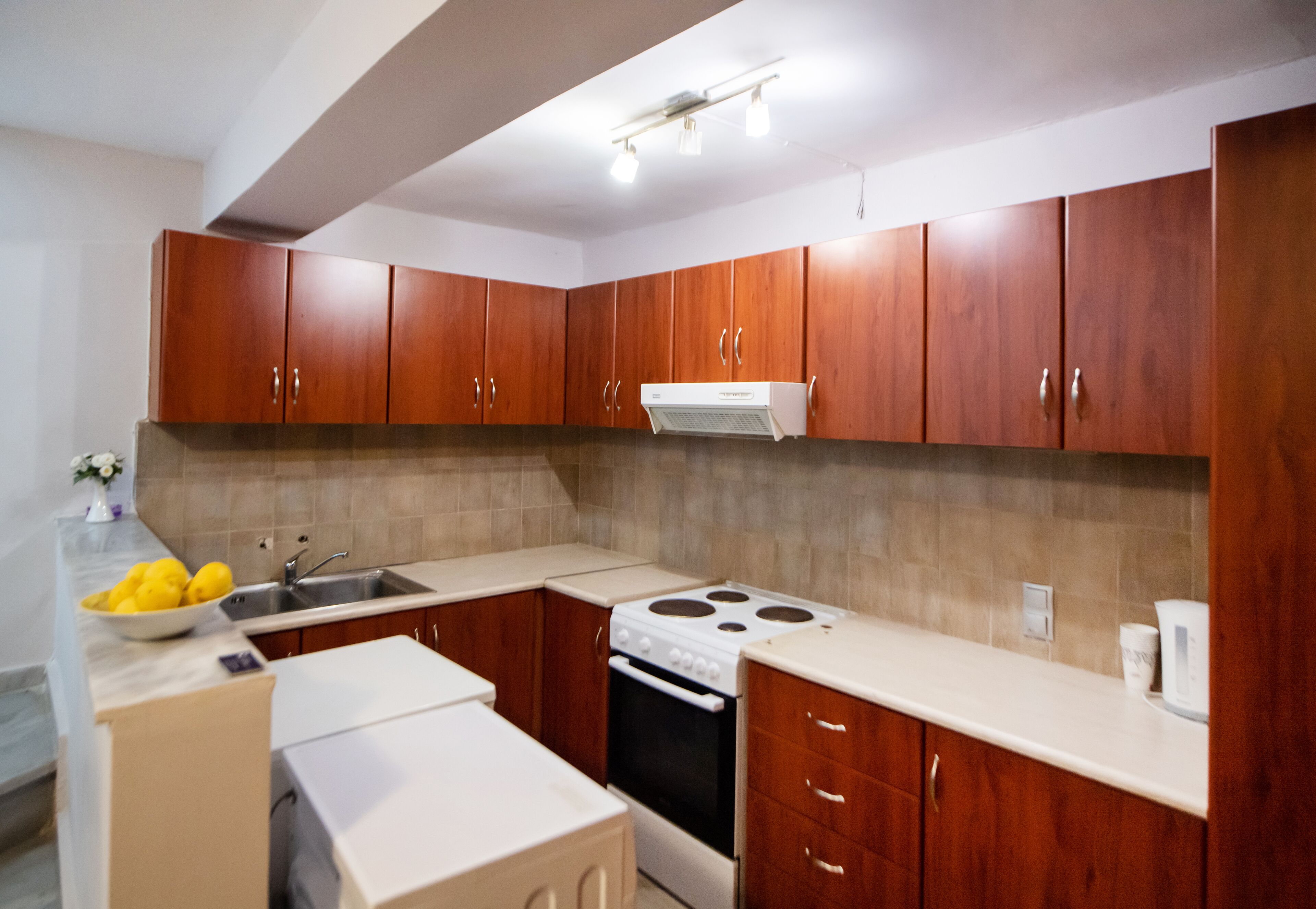 A kitchen with wooden cabinets, a stove, a sink, and a countertop with a bowl of lemons.