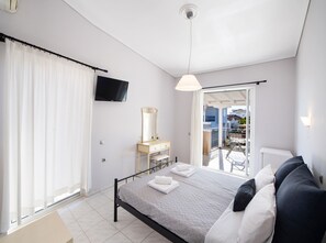 A bedroom with a bed, a dresser, a mirror, a TV, and a balcony with a view of the city. - George House (Lefkada)