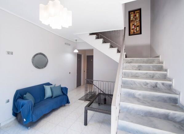A modern interior with a staircase, a blue sofa, and a wall-mounted mirror. - George House (Lefkada)