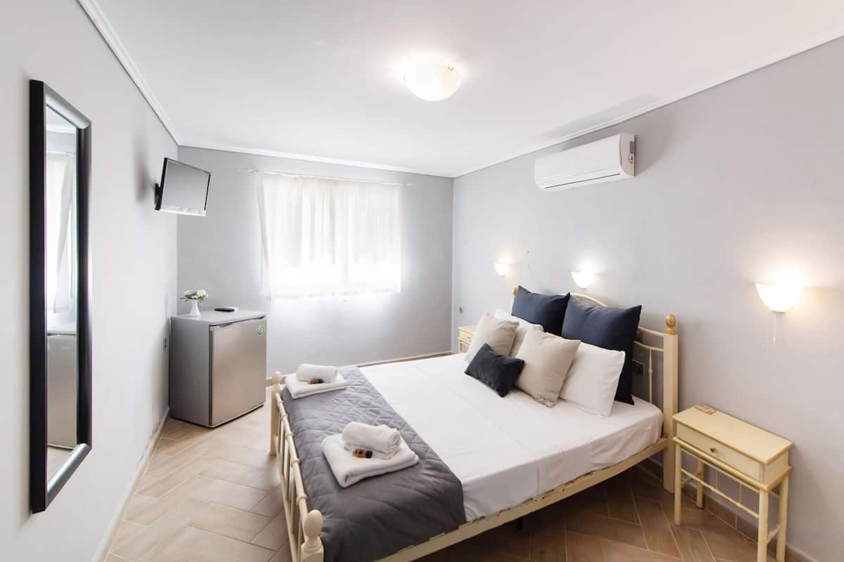 Un dormitorio con cama, mesitas de noche, un escritorio pequeño, un espejo y una ventana con cortinas.