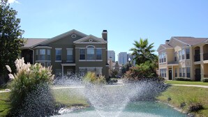 A residential area with a fountain in the center, surrounded by well-maintained lawns and mature trees. - Legacy Villa 1901 | Just a Short Walk to the Beach! (Gulfport)