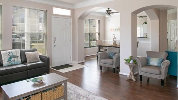 A spacious living room with a black sofa, a coffee table, and a ceiling fan. There is a kitchen area visible in the background. - Legacy Villa 1901 | Just a Short Walk to the Beach! (Gulfport)