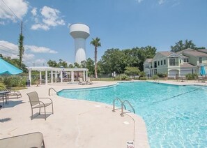 Una piscina con sillas de descanso y un pabellón, rodeada de casas y un tanque de agua.