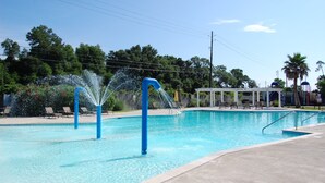 Una piscina con múltiples chorros de agua, rodeada de sillas de descanso y una zona de estar cubierta.