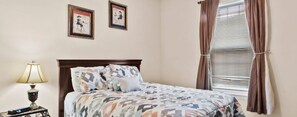 A neatly made bed with patterned bedding, a bedside lamp, and two framed pictures on the wall.