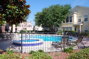 Una piscina con un jacuzzi circular, rodeada por una valla, y junto a un edificio con balcón.