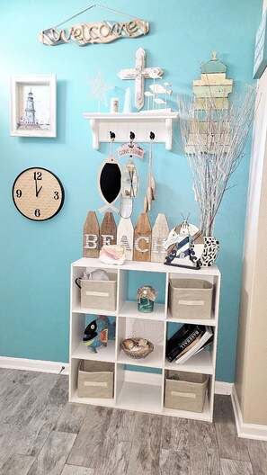 Una habitación con una pared verde azulado, un reloj, una estantería con adornos y una pintura de un faro.