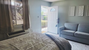 A bedroom with a bed, a grey sofa, and a door leading outside.