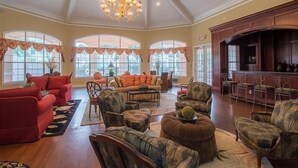 A spacious living room with a high ceiling, large windows, and a chandelier.