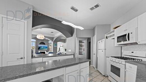 A modern kitchen with white cabinets, a granite countertop, a built-in oven, and a microwave.