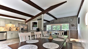 A spacious kitchen with modern appliances, a dining area with a long wooden table, and a view of the outdoors through large windows. - Breakaway House by Killington Vacation Rentals (Killington)