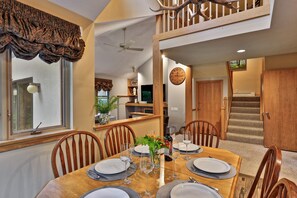 A dining area with a wooden table set for four, a clock on the wall, and a staircase leading to another level. - The Woods by Killington Vacation Rentals - 3 Bedrooms (Killington)