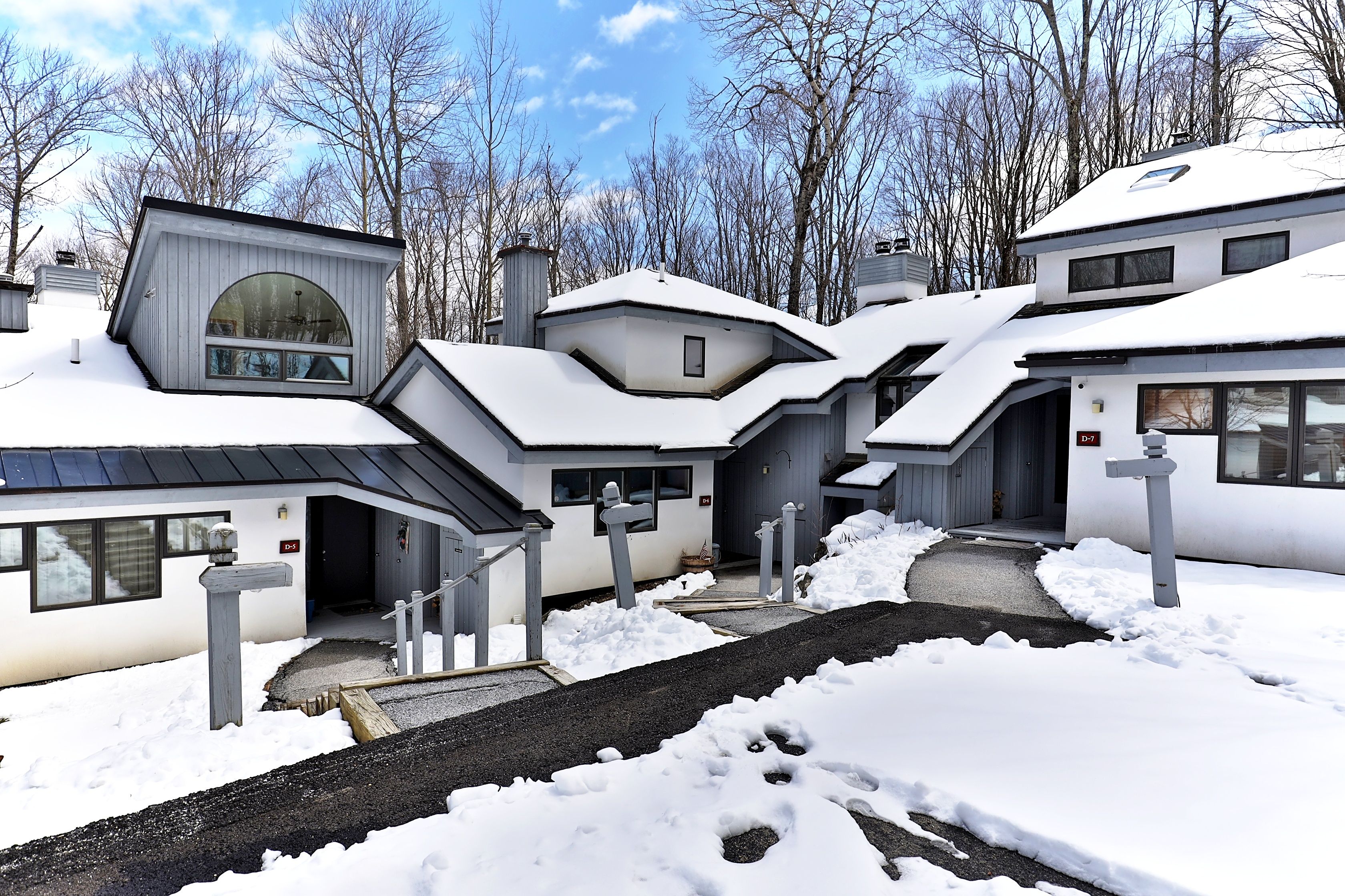 A modern residential building with multiple entry points, a covered driveway, and a snow-covered landscape.