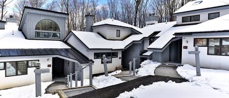A modern residential building with multiple entry points, a covered driveway, and a snow-covered landscape.