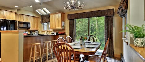 A modern kitchen with wooden cabinets, a black refrigerator, and a dining area with a wooden table and chairs.