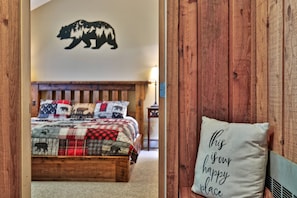 Une chambre à coucher avec un lit, une silhouette d’ours fixée au mur et un coussin orné d’une citation inspirante.