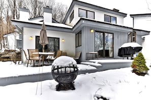 Une maison moderne à deux étages, dotée d’un patio couvert, de grandes fenêtres et surplombant un paysage enneigé.