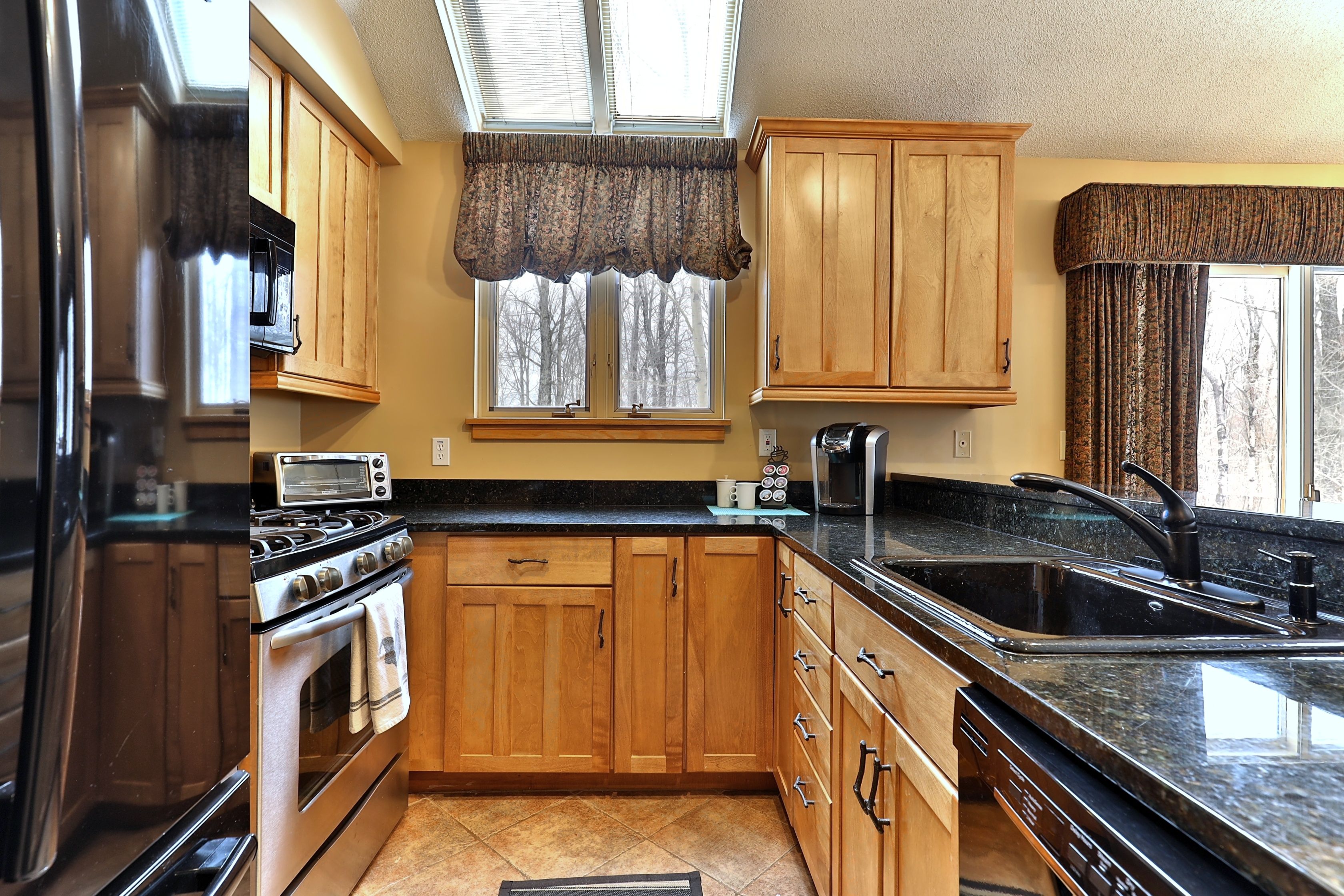 A kitchen with wooden cabinets, a stainless steel refrigerator, a stove, and a sink.