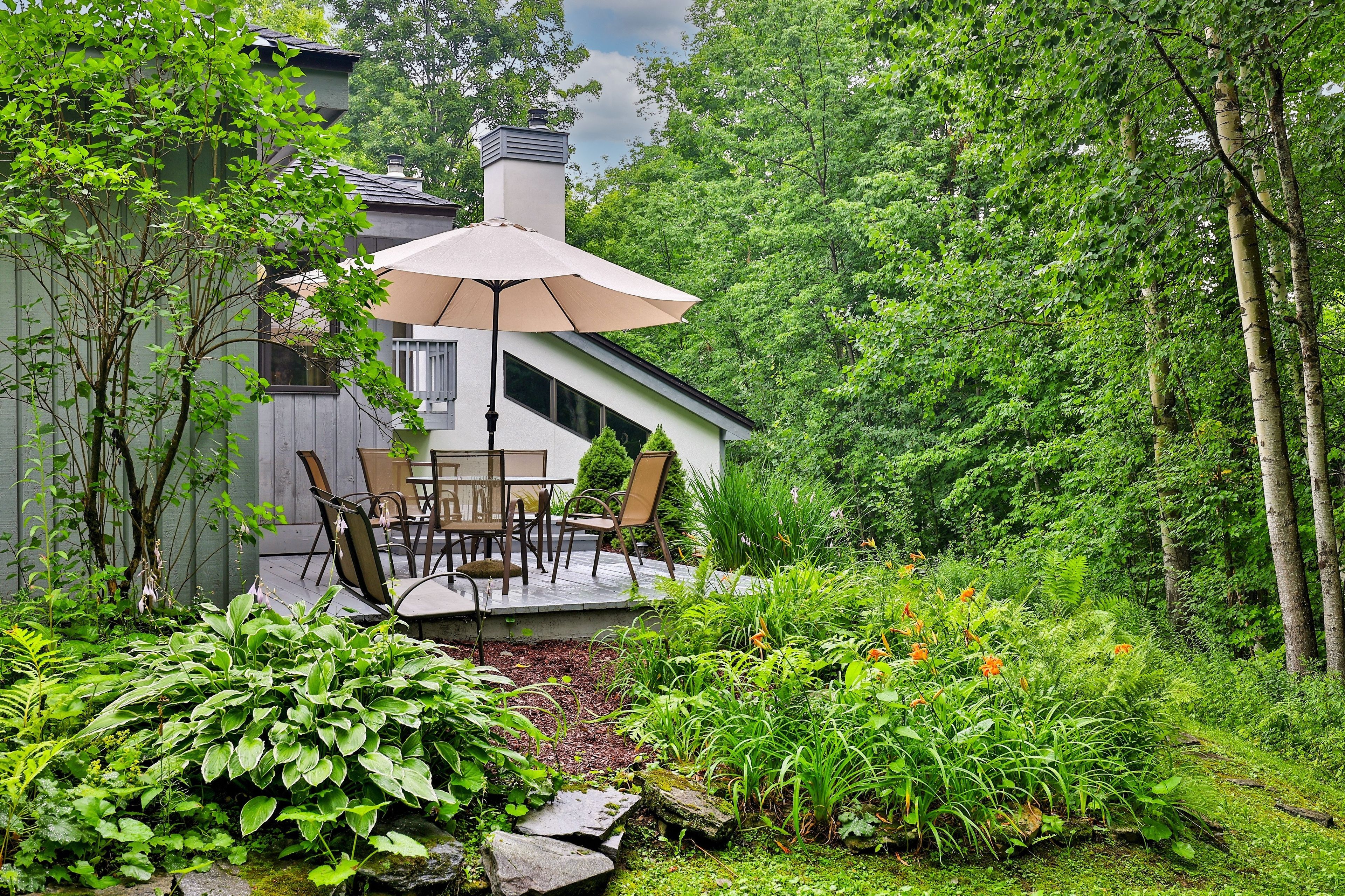 A patio with a table and chairs, surrounded by lush greenery and a wooden fence.