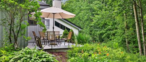 A patio with a table and chairs, surrounded by lush greenery and a wooden fence.