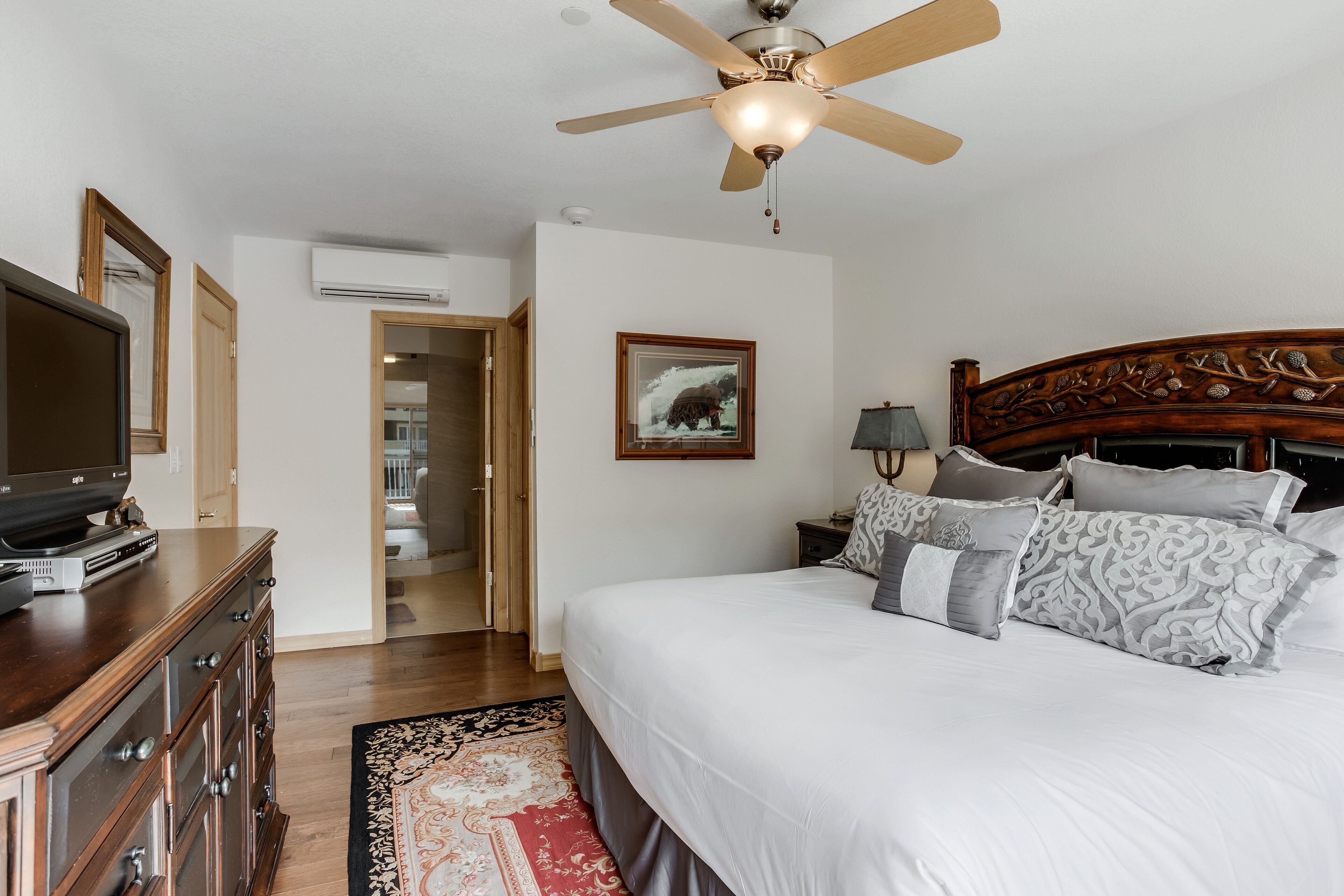 A bedroom with a bed, a ceiling fan, a television on a dresser, and a framed picture on the wall.