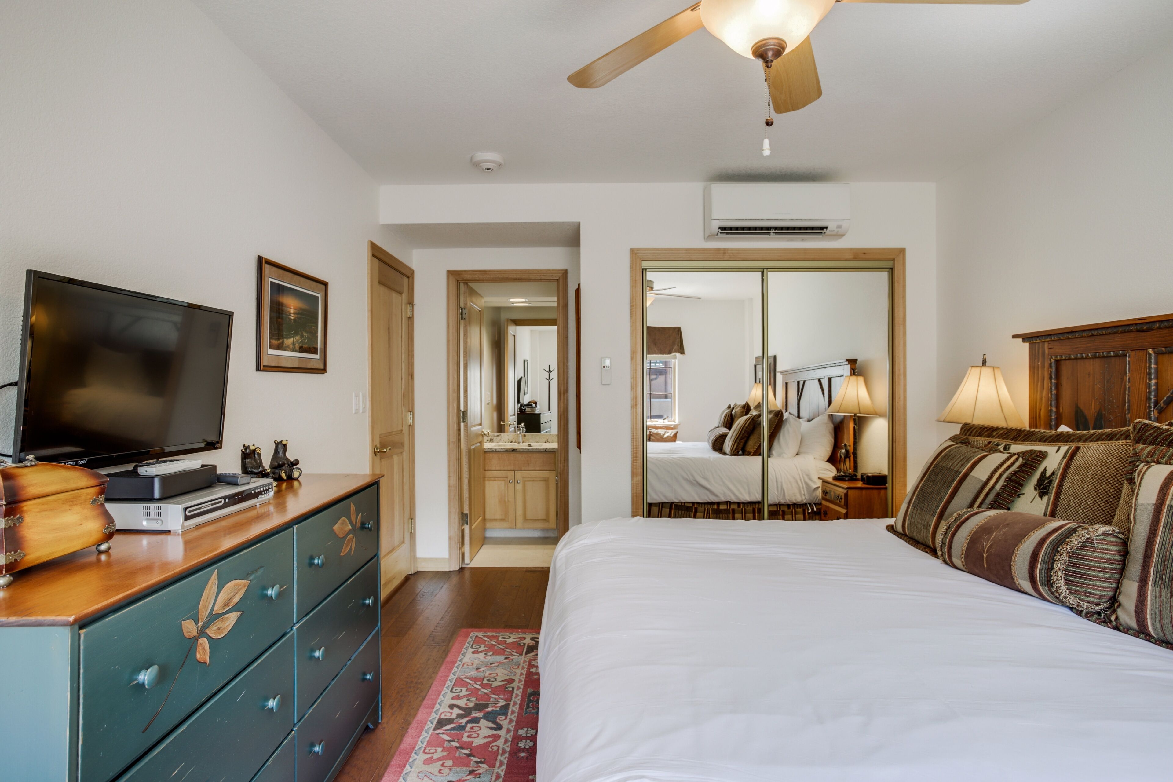 A bedroom with a bed, dresser, television, and a ceiling fan.