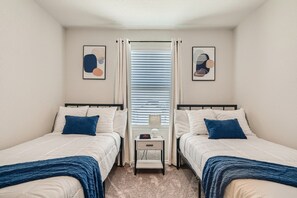 A bedroom with two beds, a nightstand, and a window with blinds.