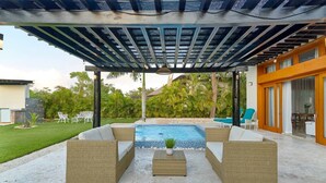 An outdoor pool area with a covered patio, lounge chairs, and a small table with a plant. - PERFECT OASIS PRIVATE POOL AND GARDEN PUNTA CANA (Punta Cana)