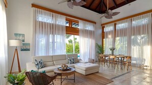 A spacious living area with a sofa, coffee table, and dining table, large windows with sheer curtains, and ceiling fans. - PERFECT OASIS PRIVATE POOL AND GARDEN PUNTA CANA (Punta Cana)