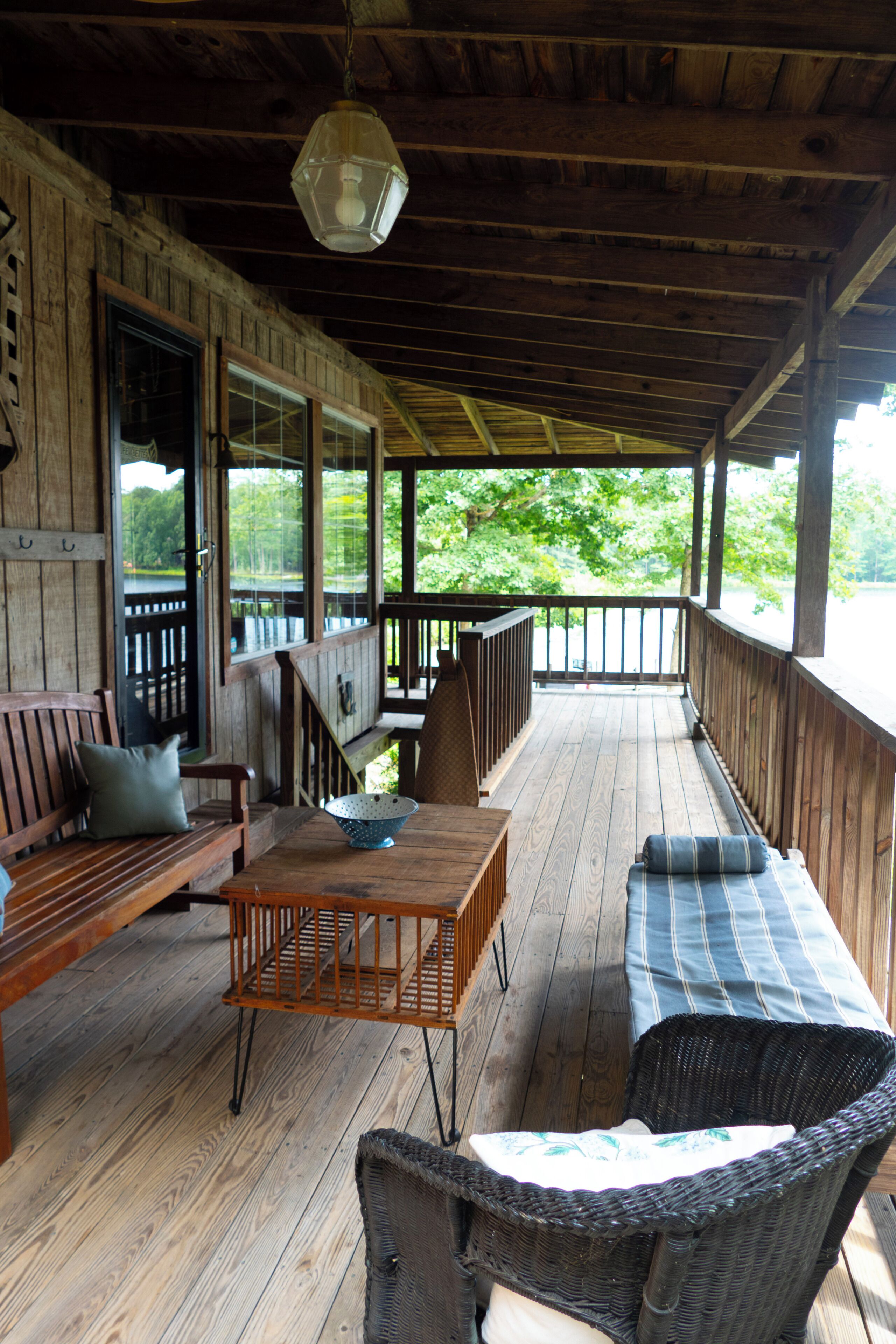 A covered porch with wooden flooring, a wooden bench, a wicker chair, and a table with a bowl.