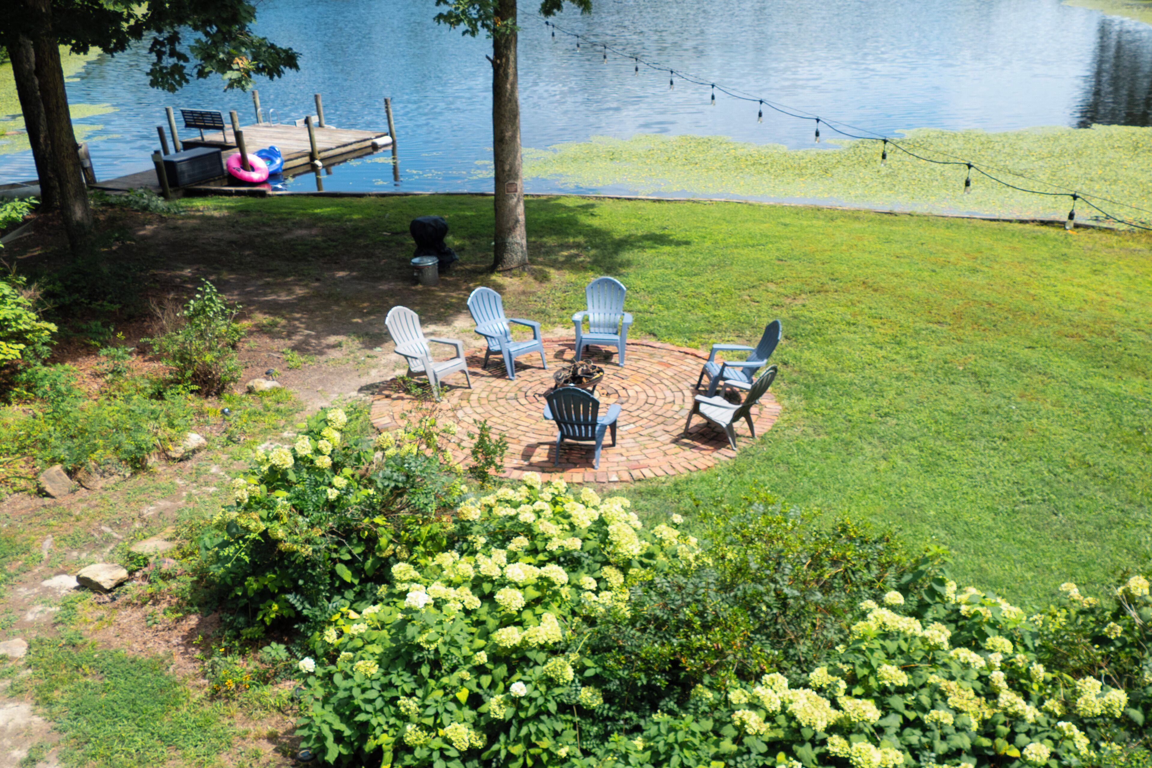 A circular outdoor seating area with chairs and a table, surrounded by a grassy lawn and a body of water.