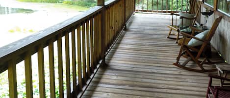 A wooden porch with a railing, a hanging light fixture, and several rocking chairs.