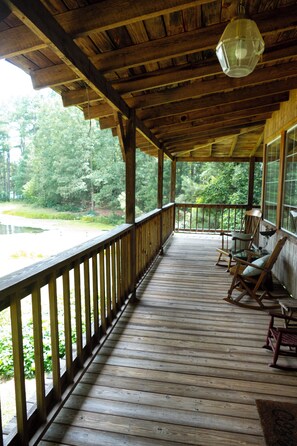 A wooden porch with a railing, a hanging light fixture, and several rocking chairs. - Your Personal Fall Retreat (Dinwiddie)