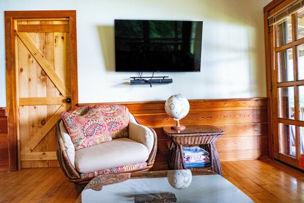 A room with a wooden door, a television mounted on the wall, a wicker chair with a patterned cushion, and a globe on a small table.