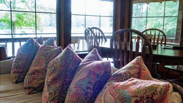 A room with a large window, a wicker sofa with patterned cushions, and a wooden table.